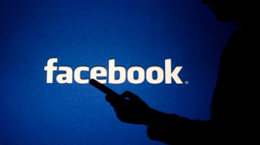 A shadowy figure using a smartphone in front of the Facebook logo