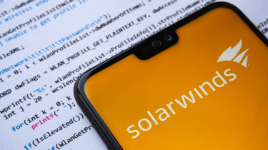 Solarwinds logo seen on the smartphone screen, with simple C attack code on the paper background.