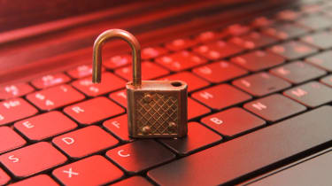 An unlocked padlock resting on a keyboard in front of a red backdrop