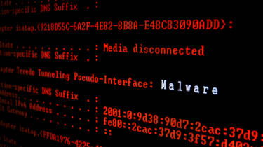 A close up image of red computer code on a black screen with the word malware displayed in white
