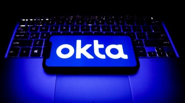 Okta company logo appearing on a smartphone which is placed upon a Windows laptop&#039;s keyboard