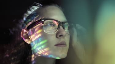 A woman wearing glasses stood in a dark room with lines of code reflected on her face