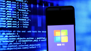 Win 11 on a smartphone in front of code on a monitor