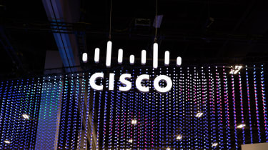 A white Cisco sign suspended from the ceiling of a dark conference room