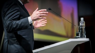 A close up of a man stood at lectern speaking at business conference